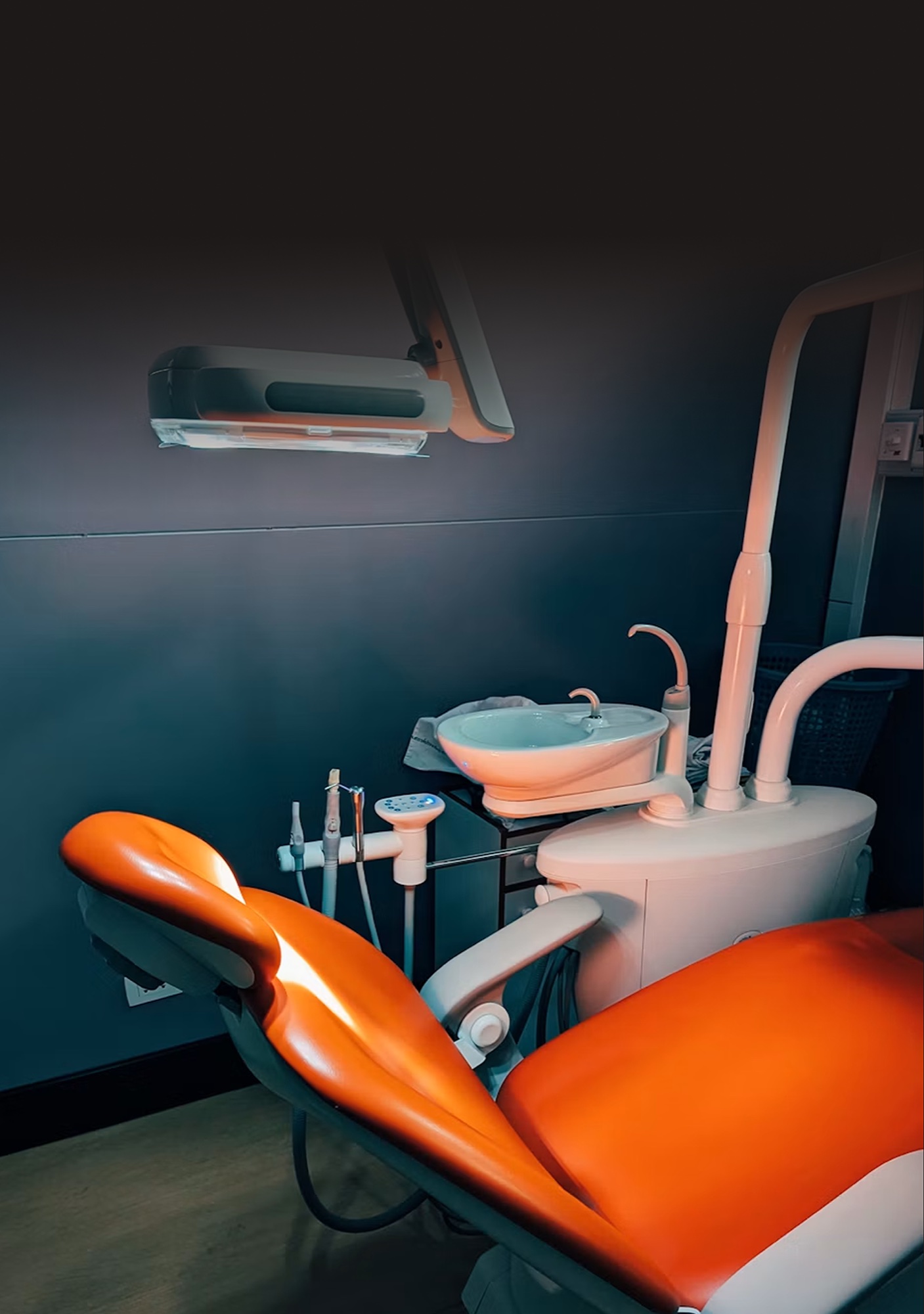An empty dental treatment room with an orange patient chair